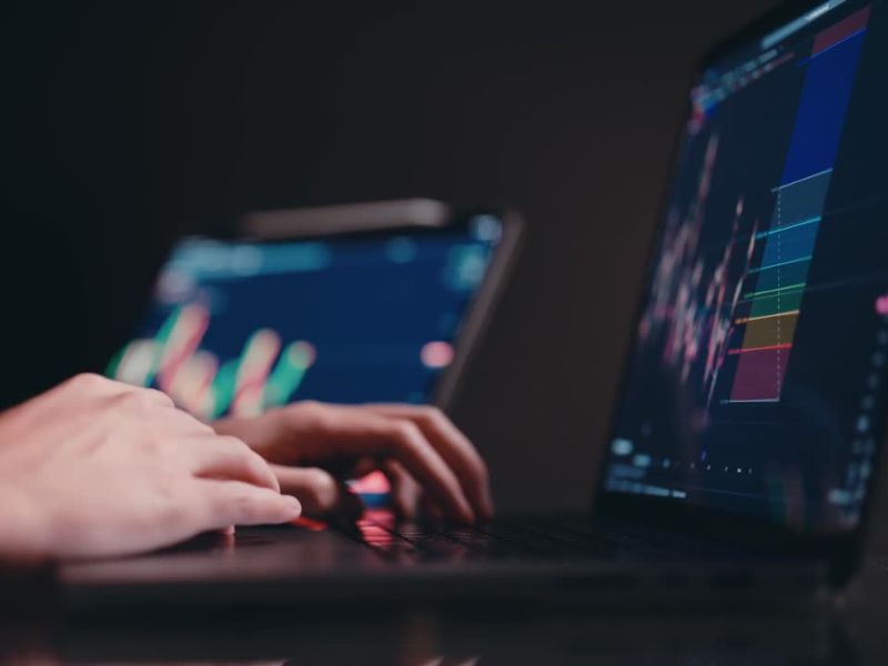 Osoba koristi laptop na kom je prikazan trading, pored njega je drugi laptop