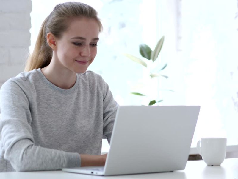Devojka u sivoj majici dugih rukava koristi laptop