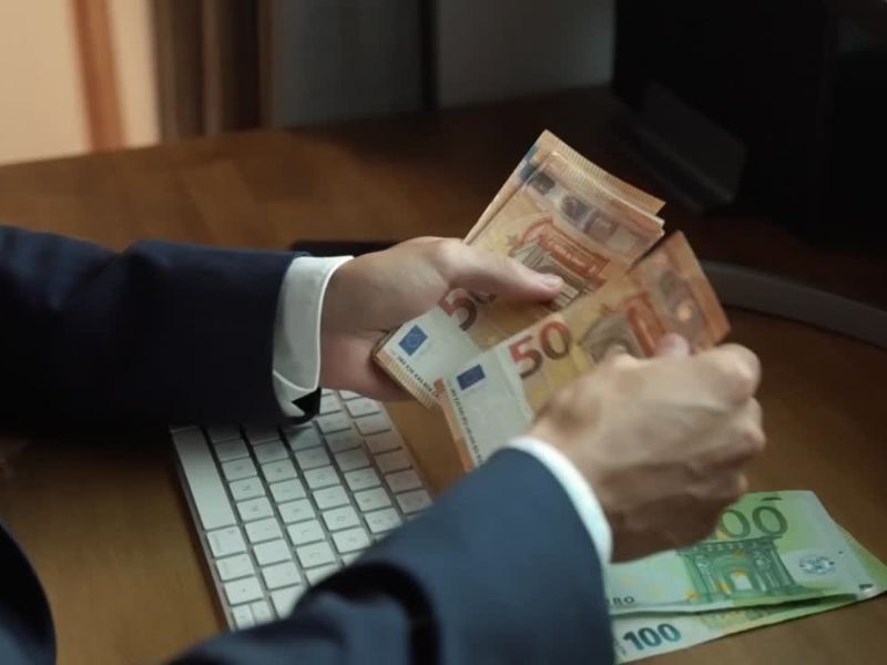 Momak u odelu sedi za kompjuterom i broji eure