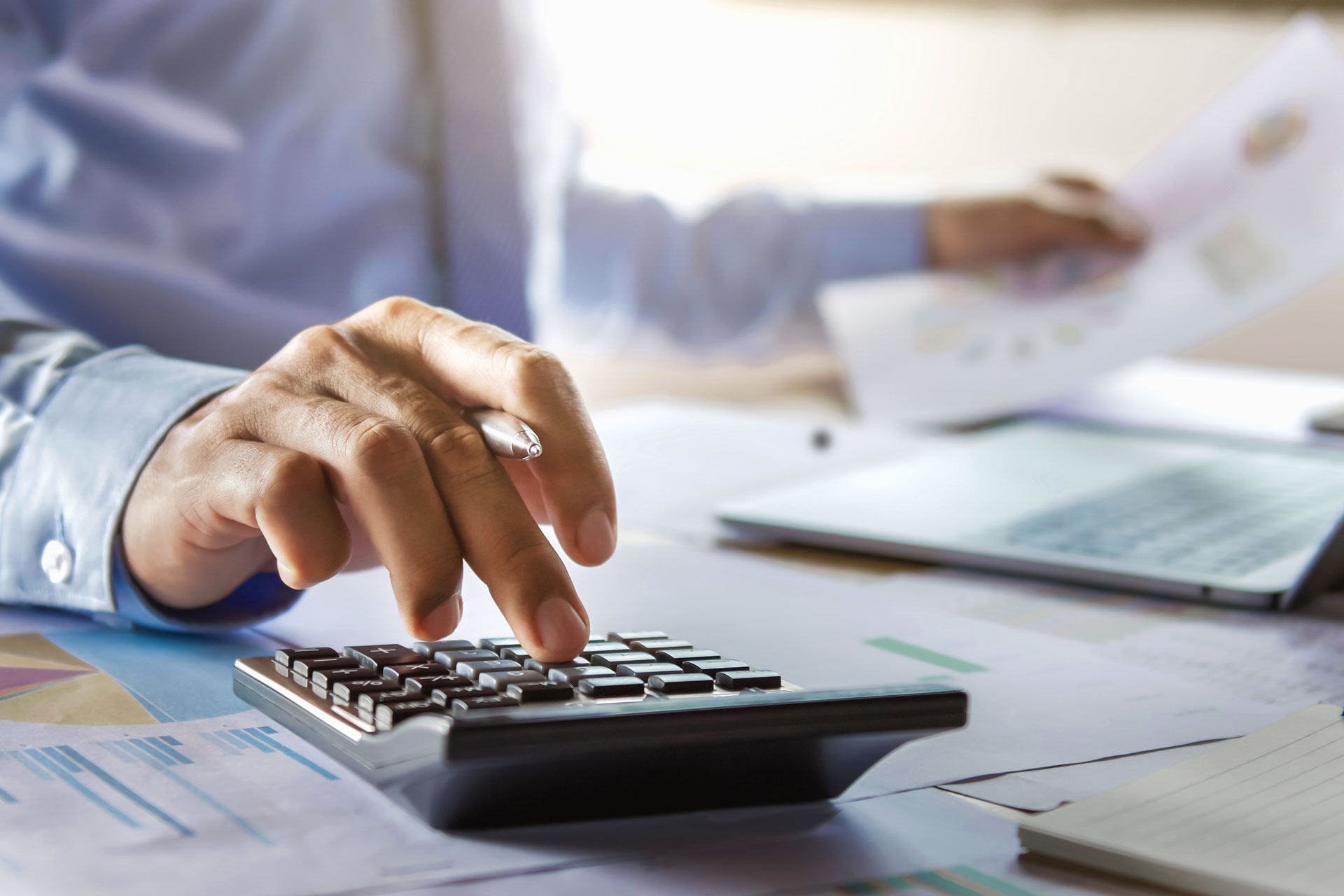 Osoba u poslovnom okruženju koristi kalkulator i analizira finansijske izveštaje na radnom stolu.