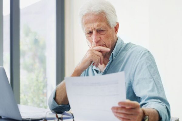 stariji čovek gleda u papire oko penzije i koristi laptop