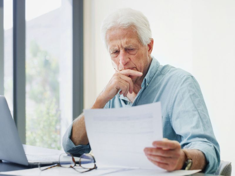 stariji čovek gleda u papire oko penzije i koristi laptop