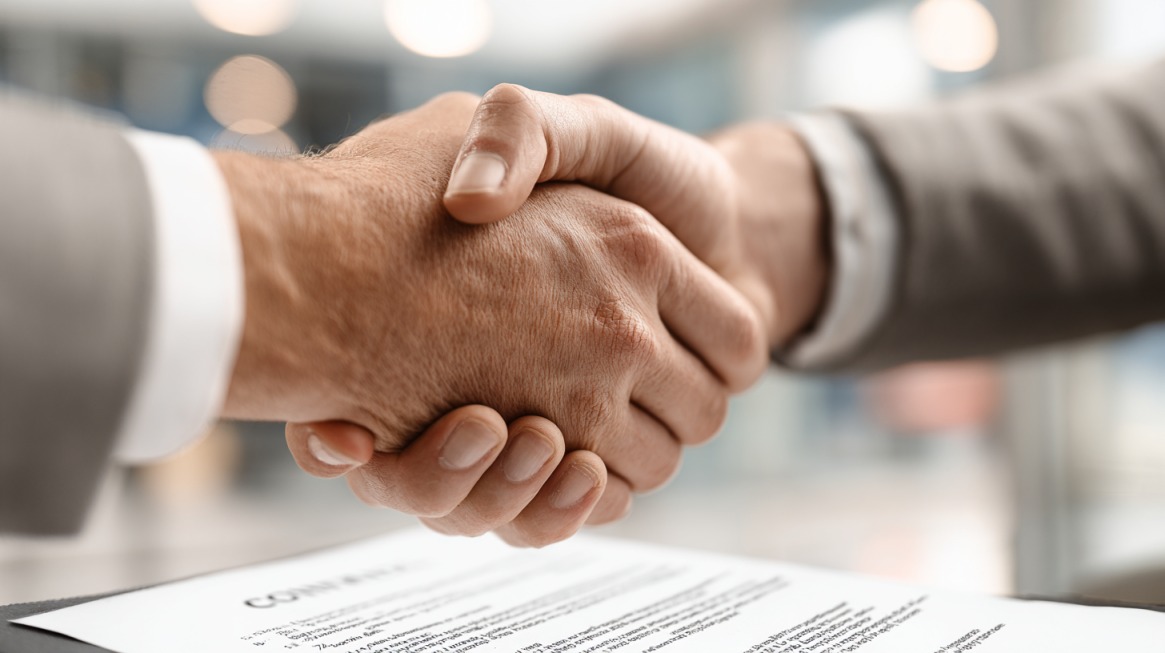 Dve osobe se rukuju iznad dokumenta koji simbolizuje potpisivanje ugovora