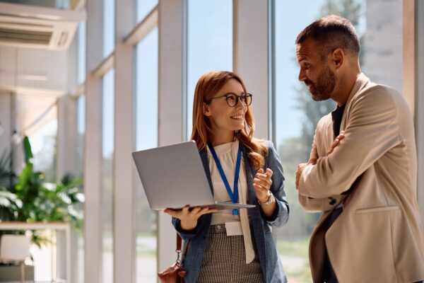 Dvoje poslovnih ljudi razgovaraju u kancelariji dok koriste laptop, simbol svakodnevnog upravljanja firmom i finansijske podrške