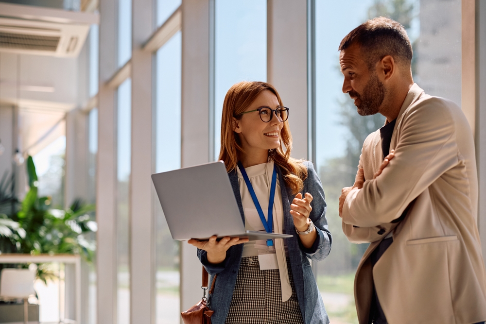 Dvoje poslovnih ljudi razgovaraju u kancelariji dok koriste laptop, simbol svakodnevnog upravljanja firmom i finansijske podrške