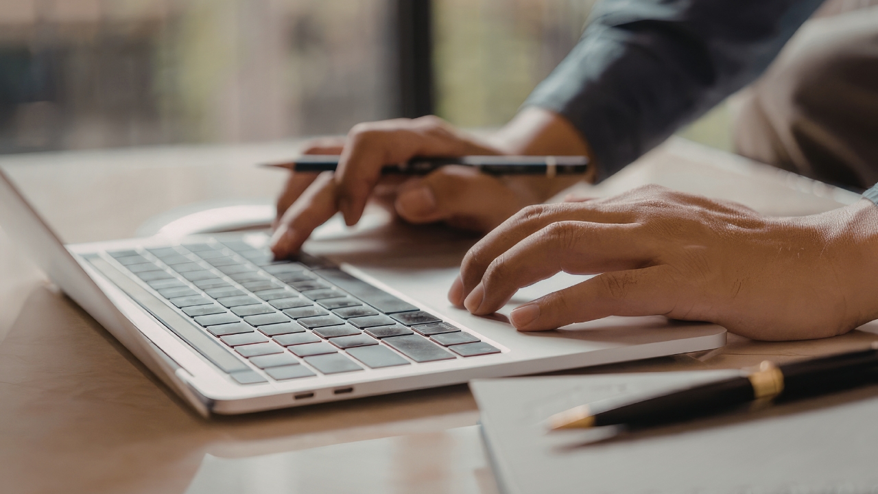 Ruke osobe koja proverava podatke o doprinosima na laptopu uz beleške na stolu