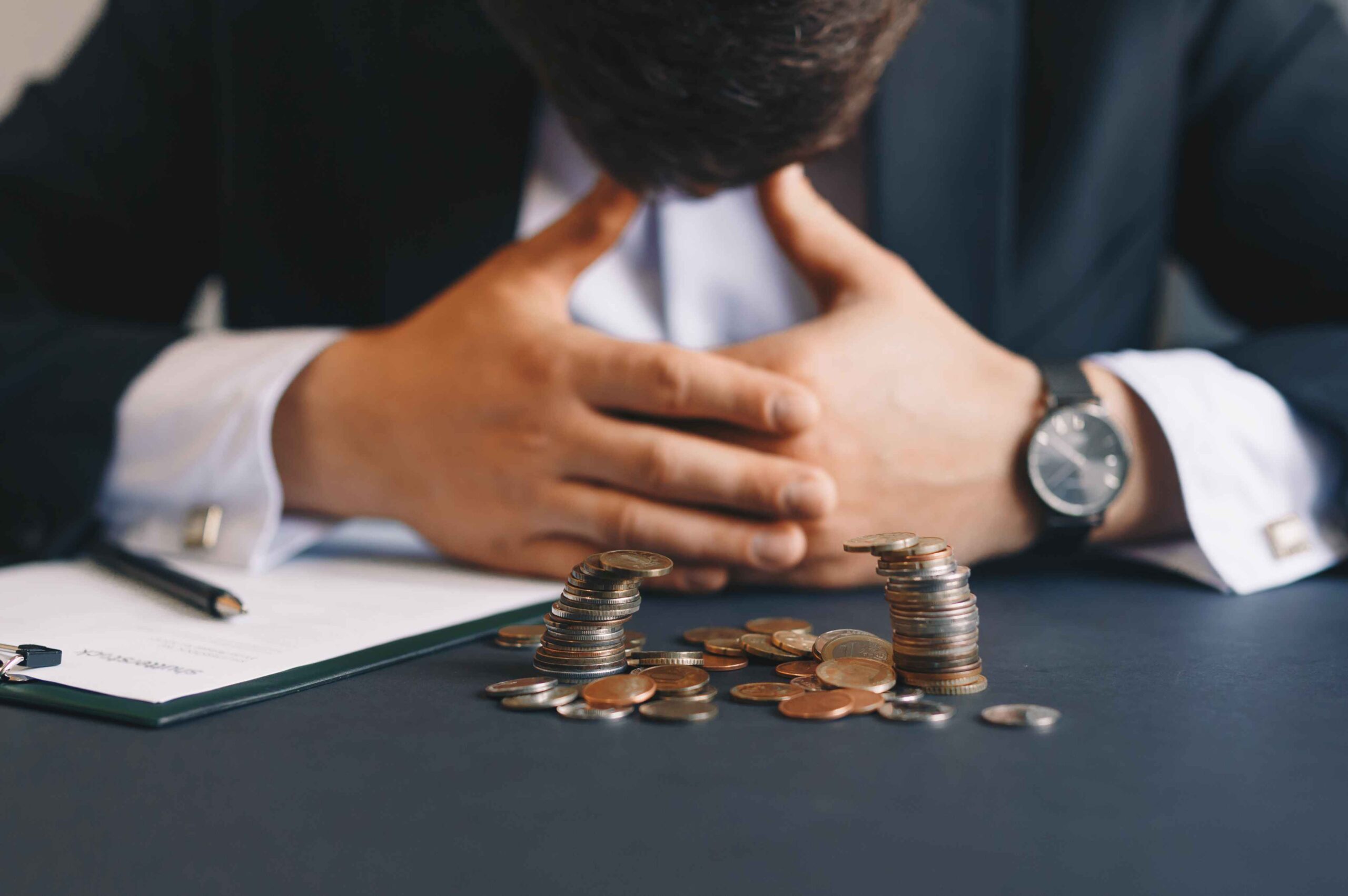 Zabrinut muškarac sa spuštenom glavom pored gomile novčića na stolu