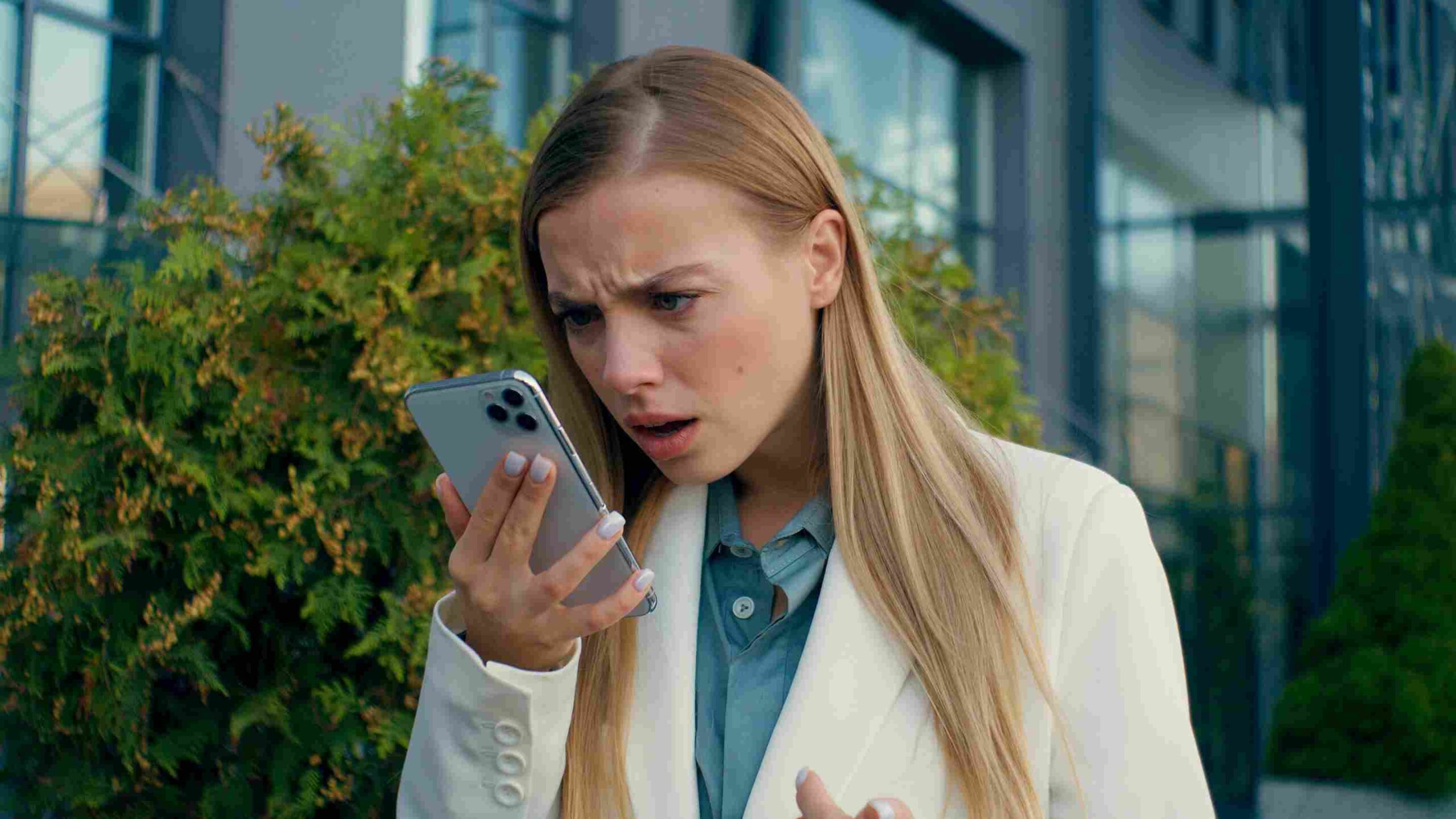 Žena zabrinuto gleda u telefon ispred poslovne zgrade