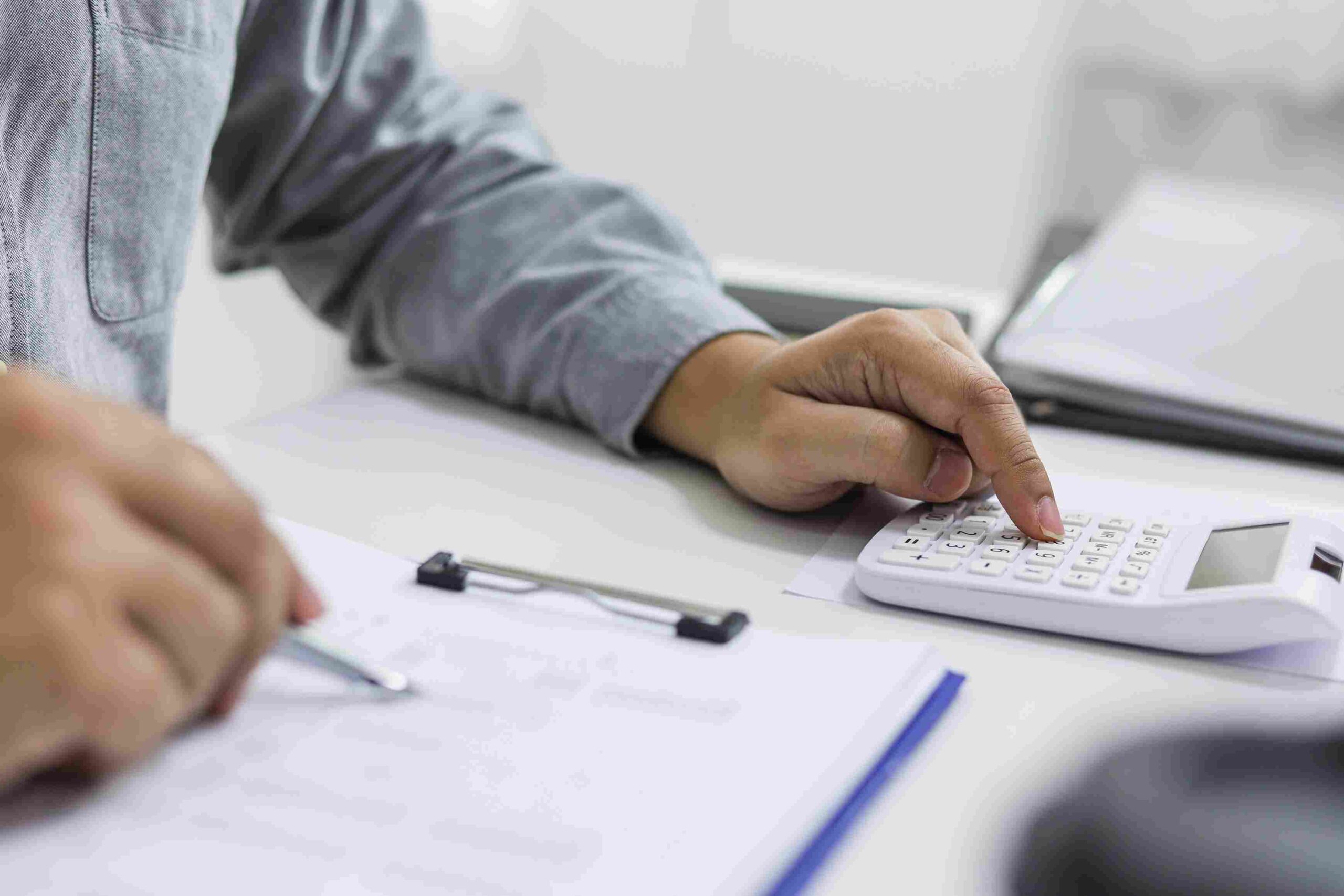 Osoba koristi digitron i popunjava dokumente na stolu