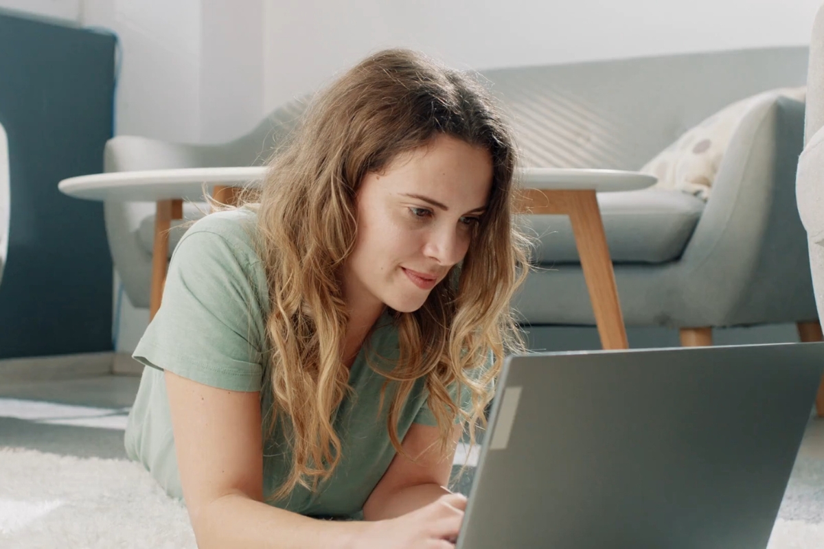 devojka gleda nešto na laptopu i leži na podu