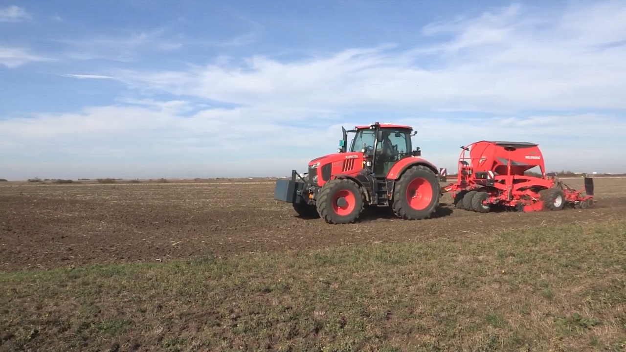 Crveni traktor sa sejalicom obrađuje veliku poljoprivrednu parcelu