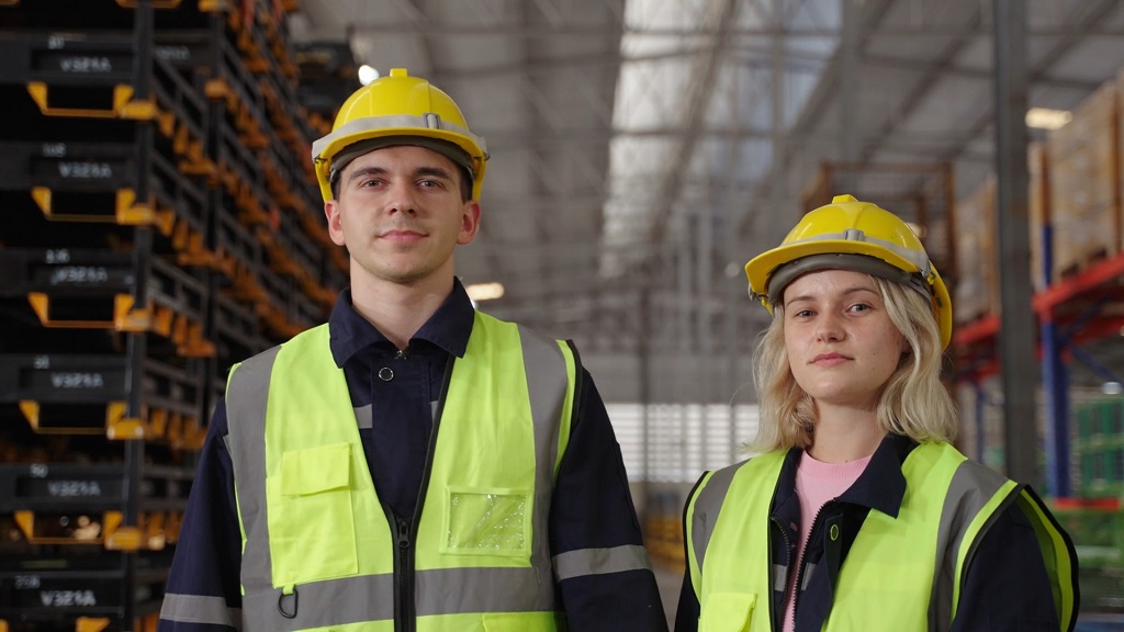 Zaposleni sa zaštitnim kacigama i reflektujućim prslucima u industrijskom skladištu