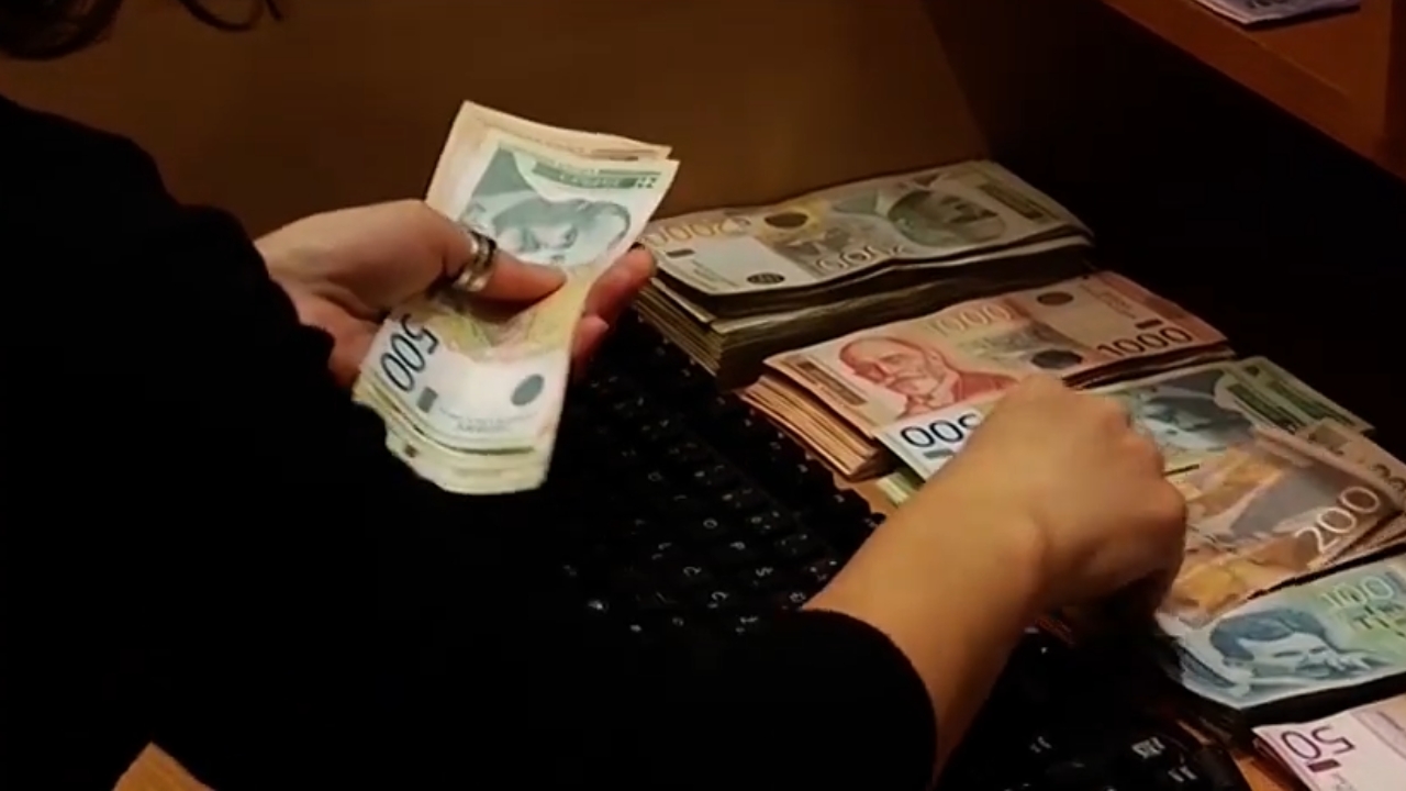 Osoba broji svežnjeve dinarskih novčanica na stolu.