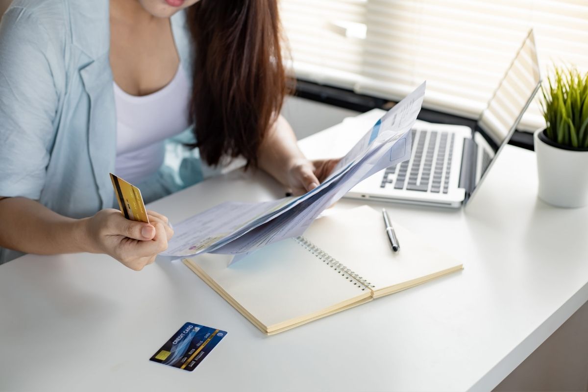 devojka gleda u dokumentaciju i u kreditnu karticu, na stolu notes, hemijska i laptop