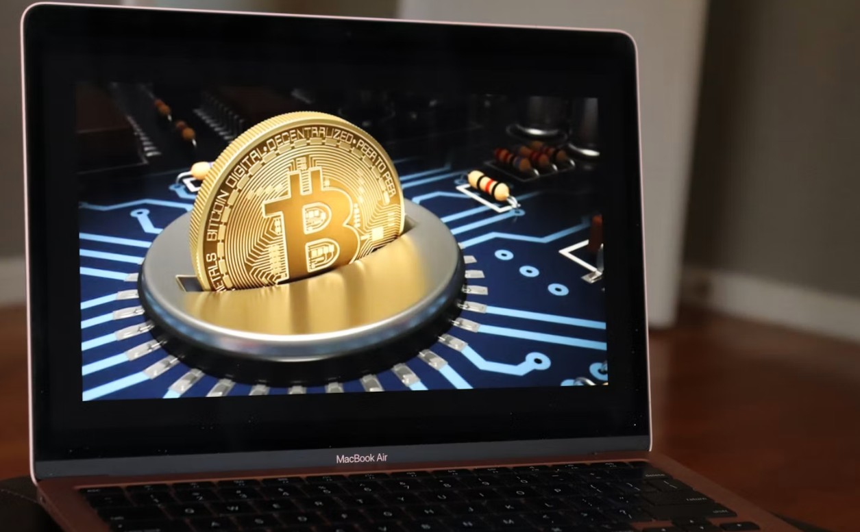 Laptop sa prikazom Bitcoin novčića na ekranu i elektronskim komponentama u pozadini