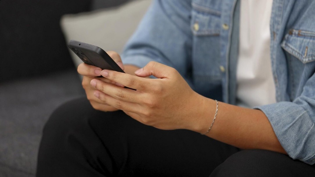 Osoba drži telefon i čita SMS poruku povezanu sa lažnim obaveštenjem o dostavi paketa
