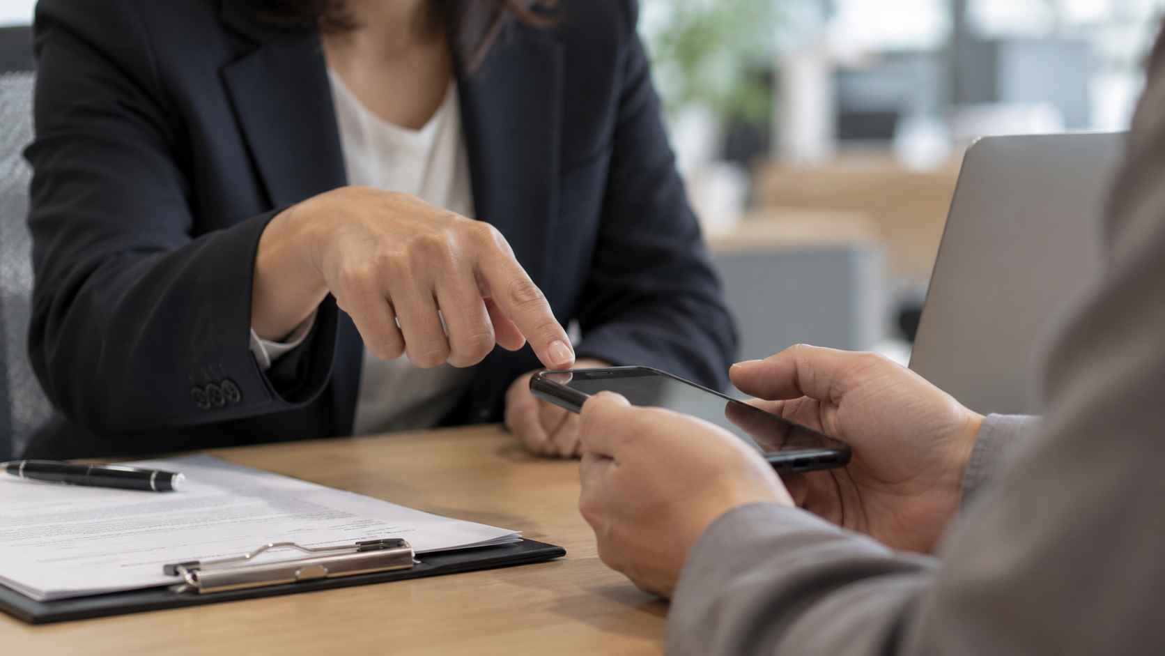 Bankarski službenik pokazuje klijentu informacije na telefonu tokom razgovora o pogrešnoj uplati.